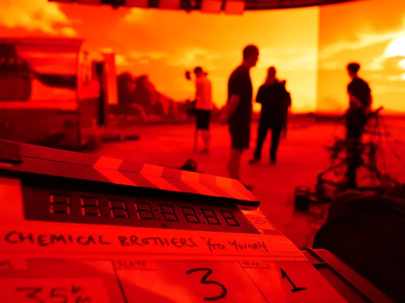 Crew silhouetted against a red-lit LED volume during the ‘Live Again’ shoot, with the clapperboard in the foreground.